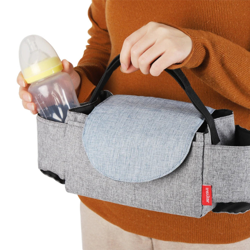 Person holding a baby carrier with a bottle pocket, wearing an orange sweater.