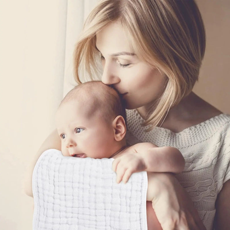 Woman holding a baby wrapped in a white blanket against a neutral background
