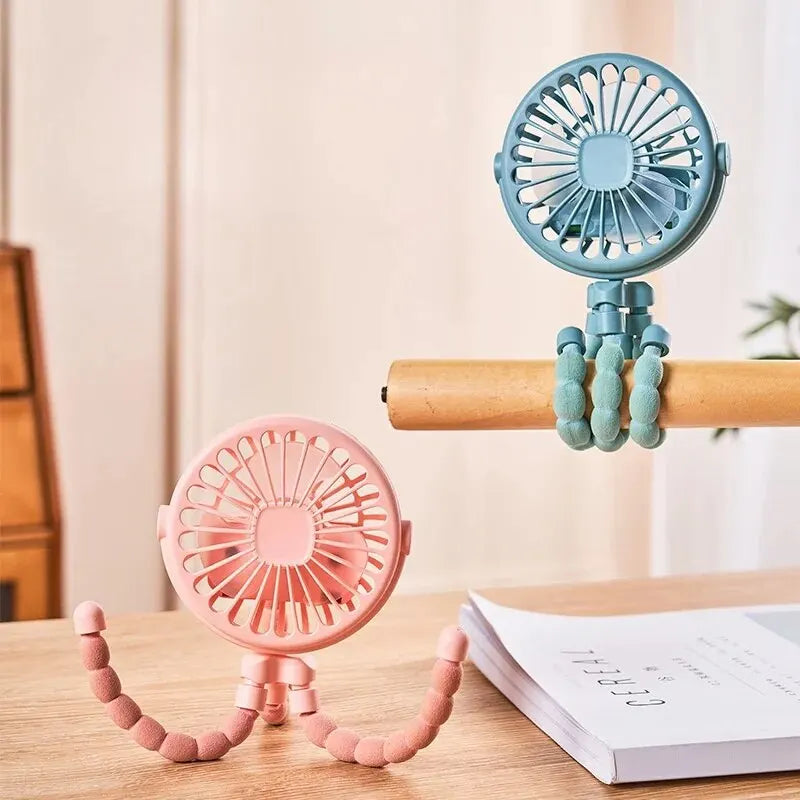 Two portable fans, one pink and one blue, on a wooden surface with a neutral background.